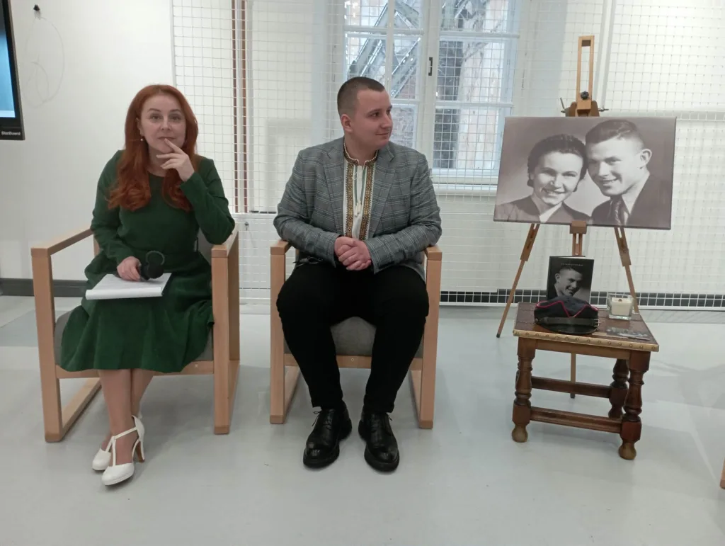 Двоє людей сидять поруч на виставці з фото.