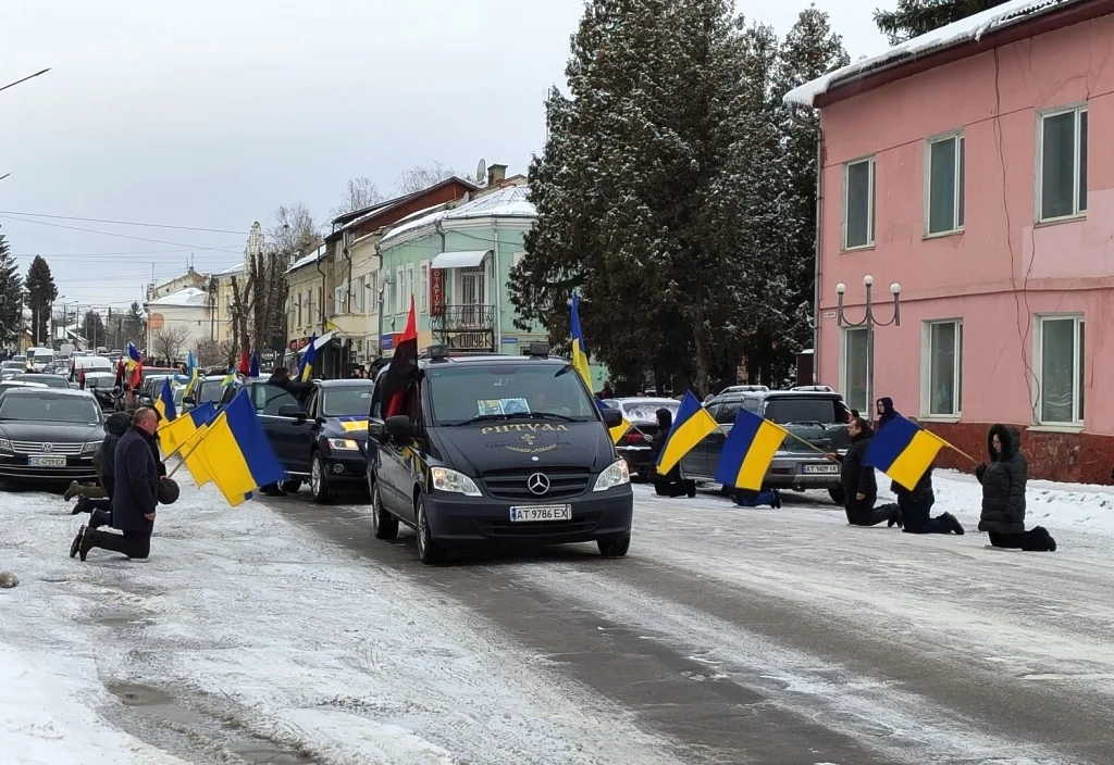 Похоронна процесія з українськими прапорами на зимовій вулиці