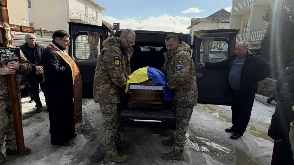 Військові несуть труну, накриту українським прапором