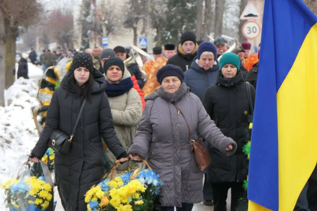 Люди несуть квіти на похорон з українським прапором