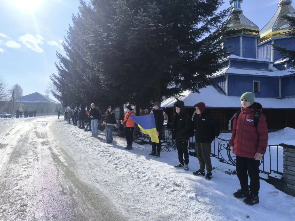 Люди стоять зі прапором України біля церкви взимку