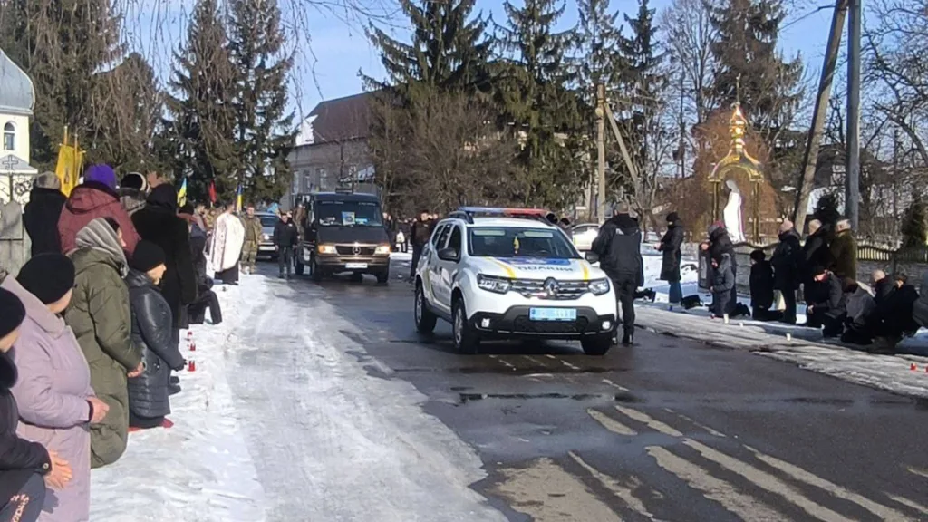 Люди стоять вздовж дороги з поліцейським авто взимку