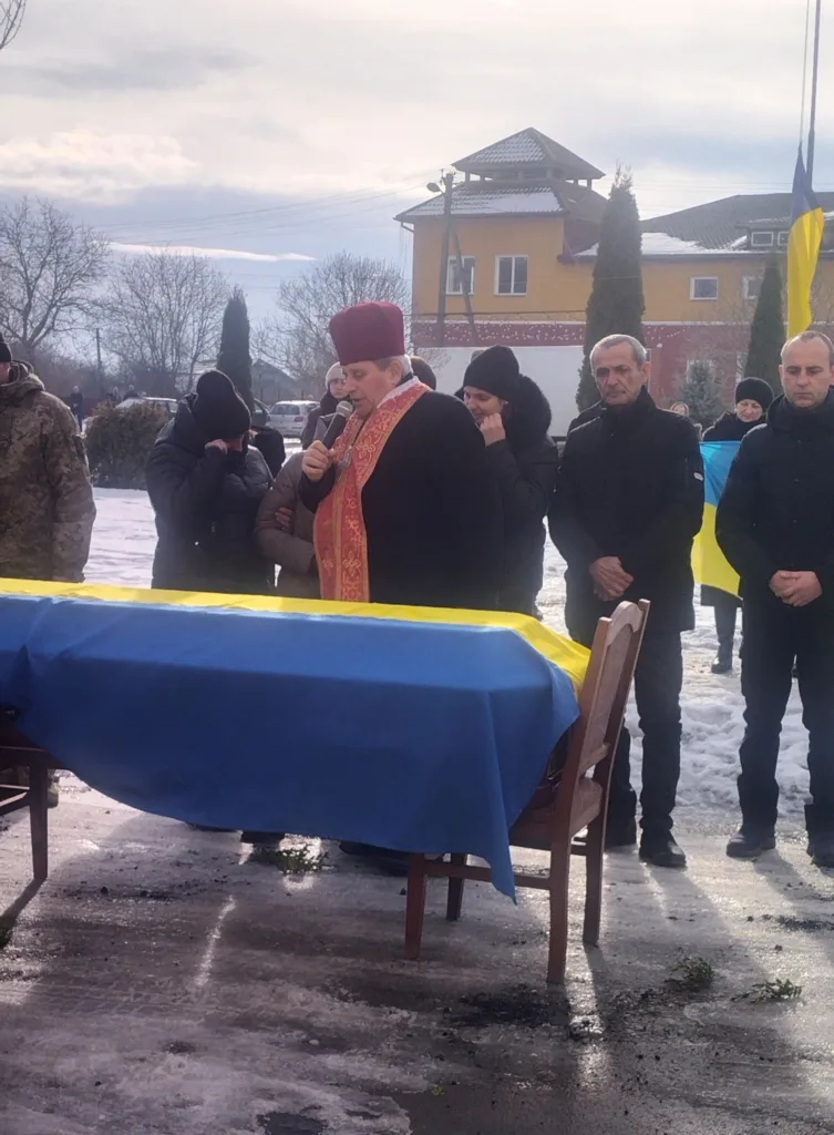 Священник молиться біля труни, накритої українським прапором