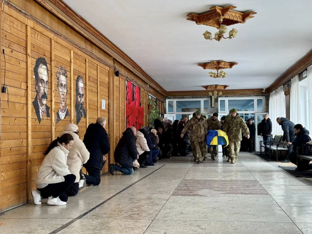 Військові несуть труну, люди стоять на колінах