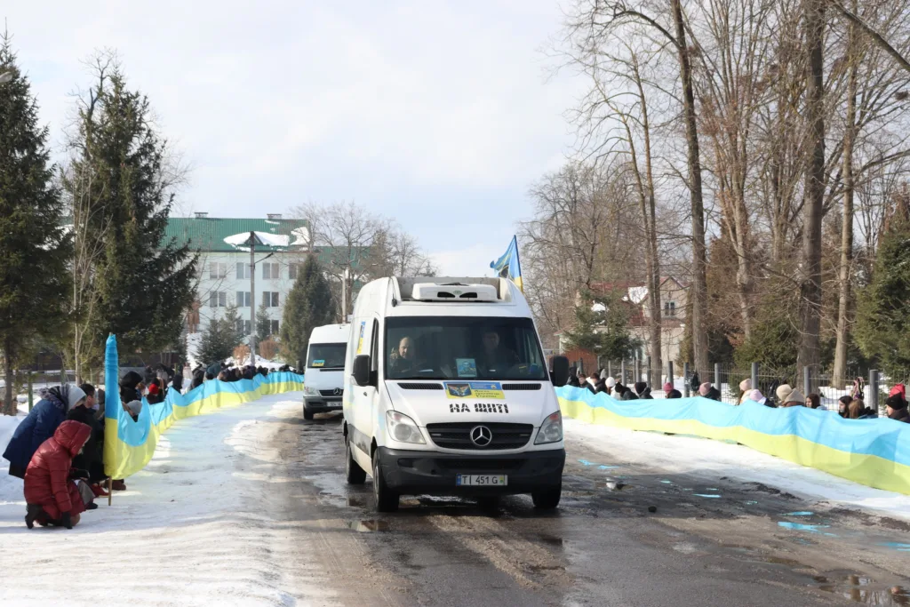 Люди з українським прапором вітають автоколону