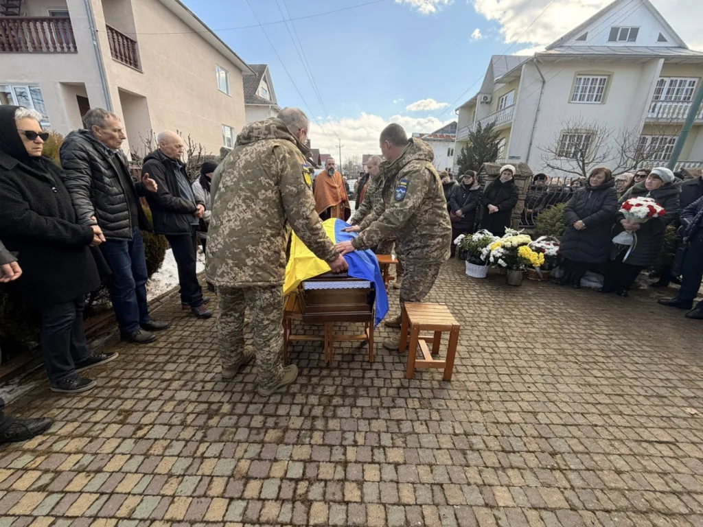 Військові накривають труну українським прапором на похороні