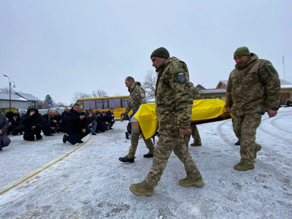 Військові несуть труну, люди стоять на колінах