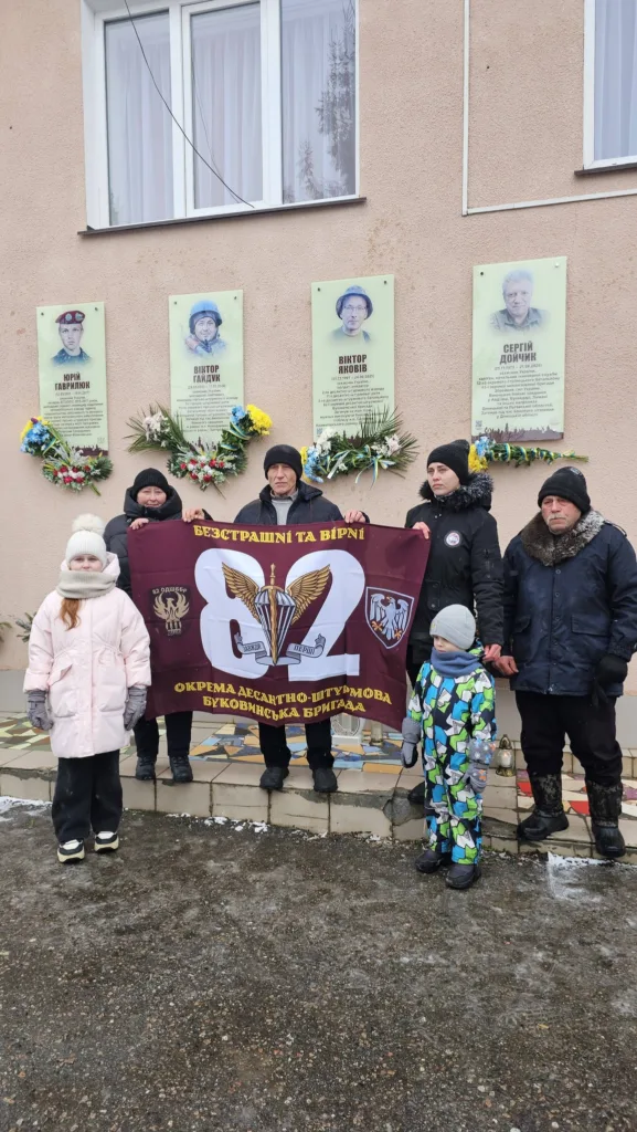 Люди тримають прапор біля меморіальних дощок героїв