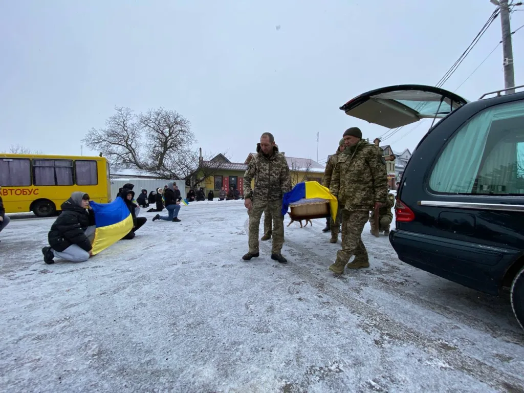 Військові несуть домовину, люди тримають український прапор