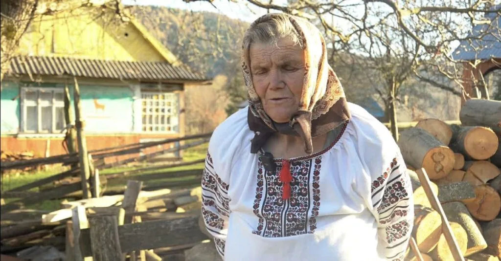 Жінка в українській вишиванці біля дерев’яного подвір’я