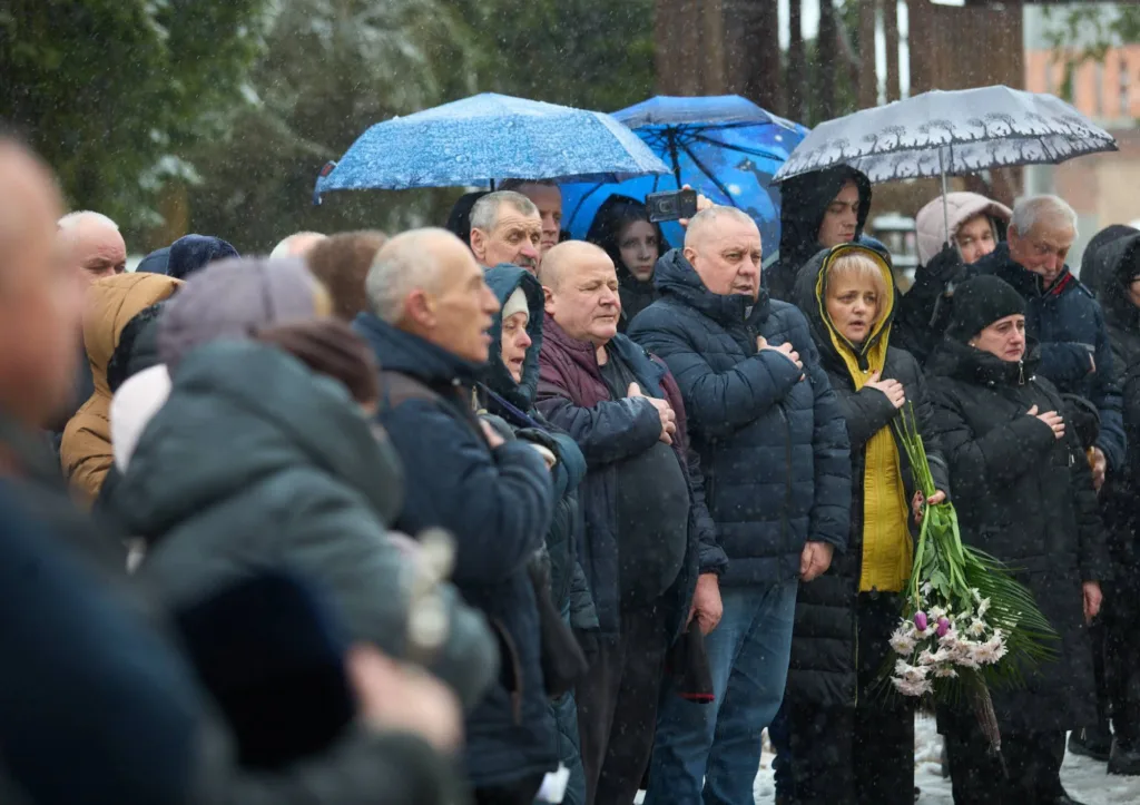 Люди стоять під дощем із квітами та парасольками