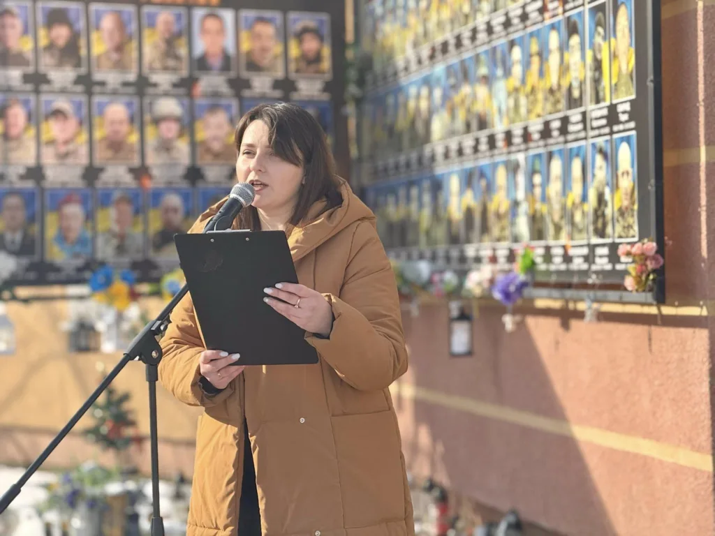 Жінка говорить біля меморіальної стіни героїв