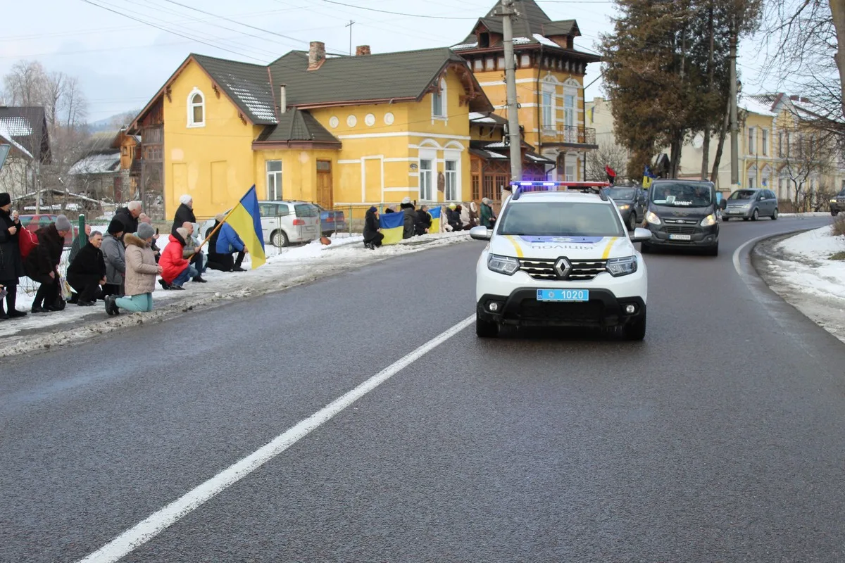 Поліцейська машина їде вулицею біля людей з прапорами