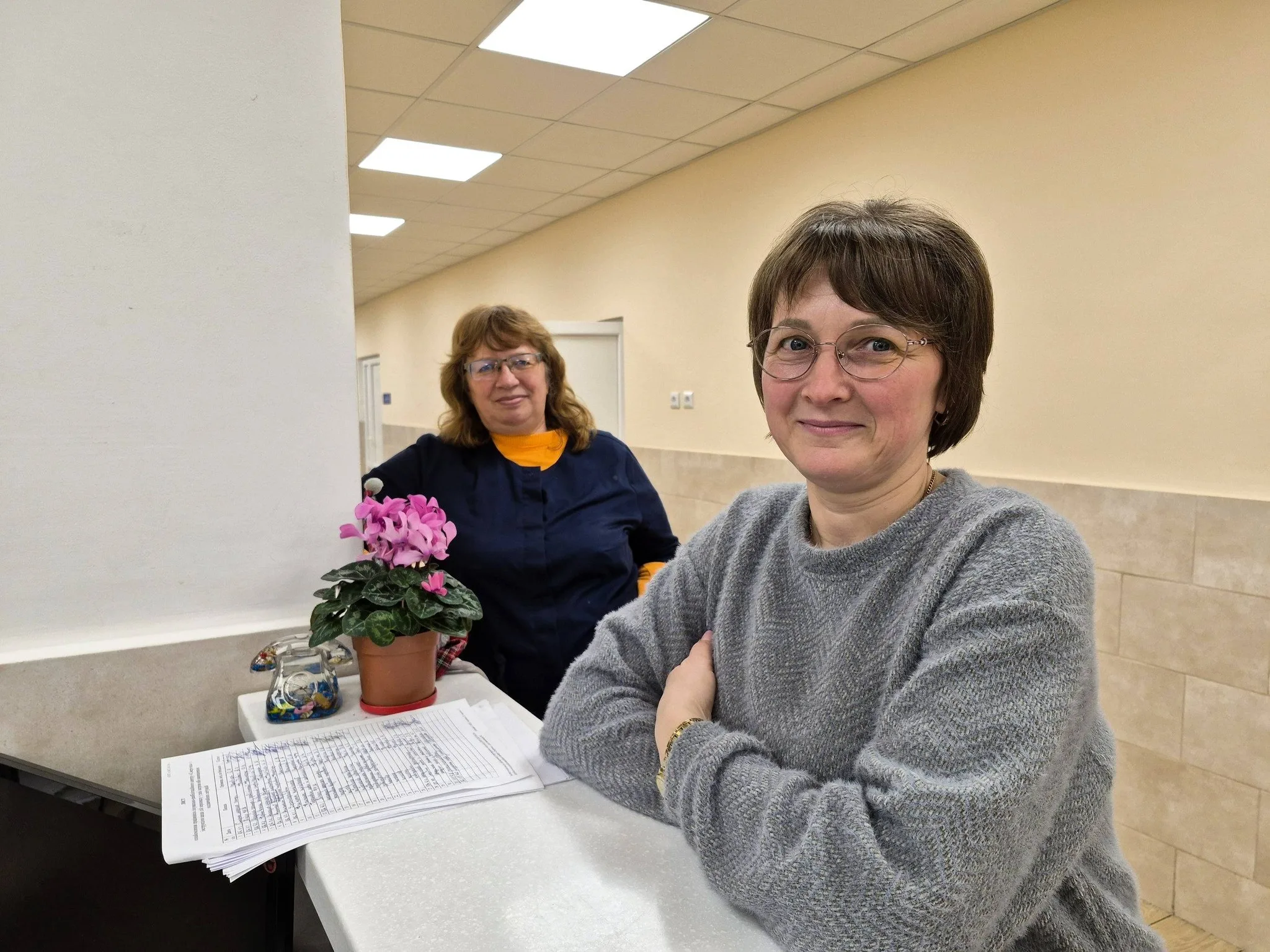 Дві жінки у коридорі біля столу з квіткою