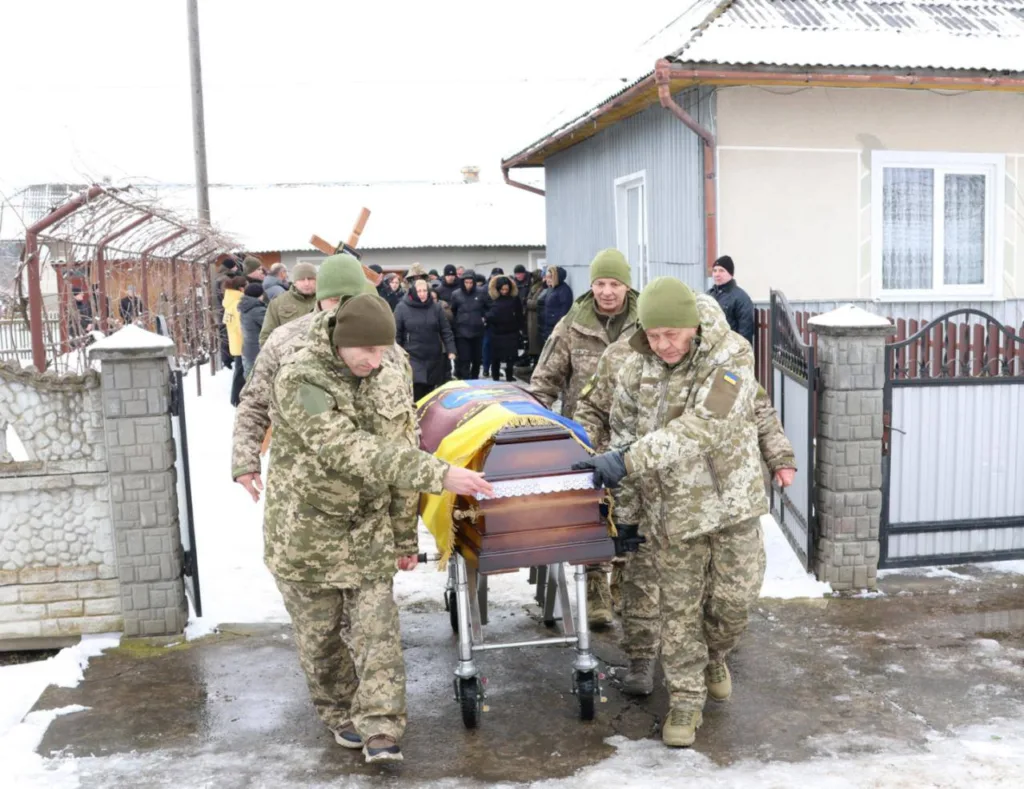 Військові несуть труну, покриту українським прапором