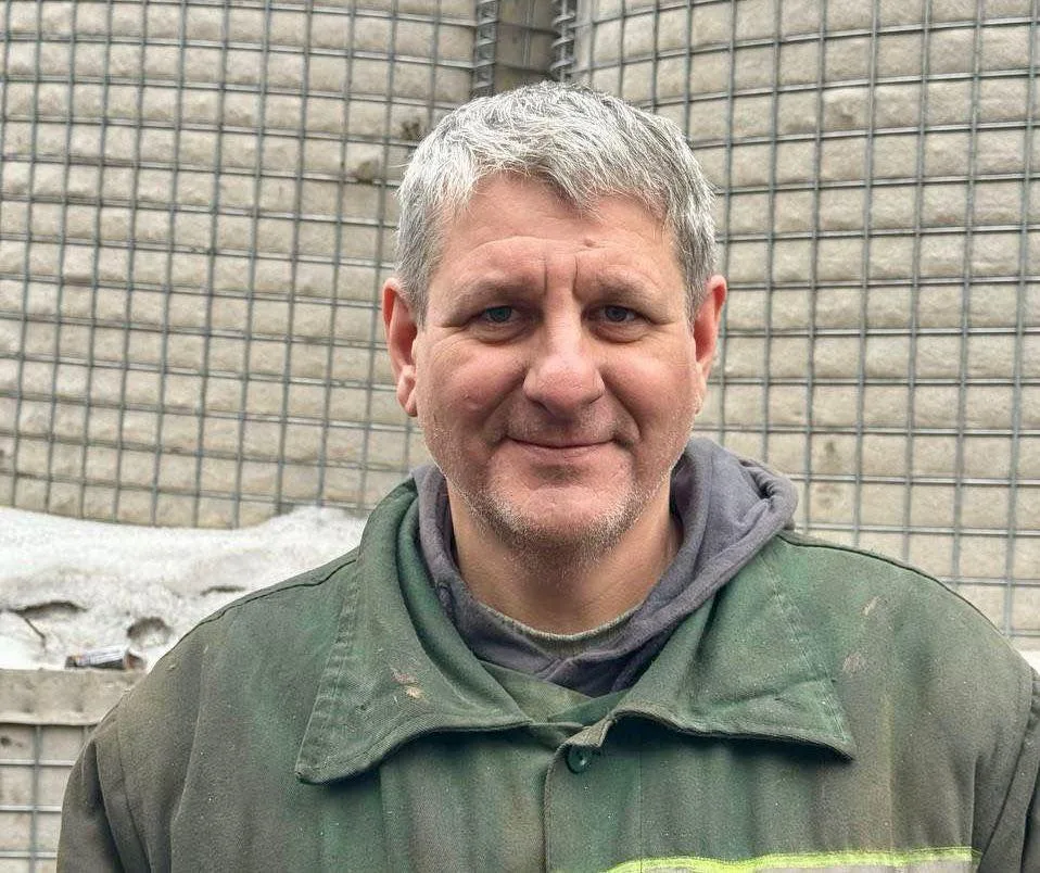 Чоловік у зеленій куртці посміхається на вулиці