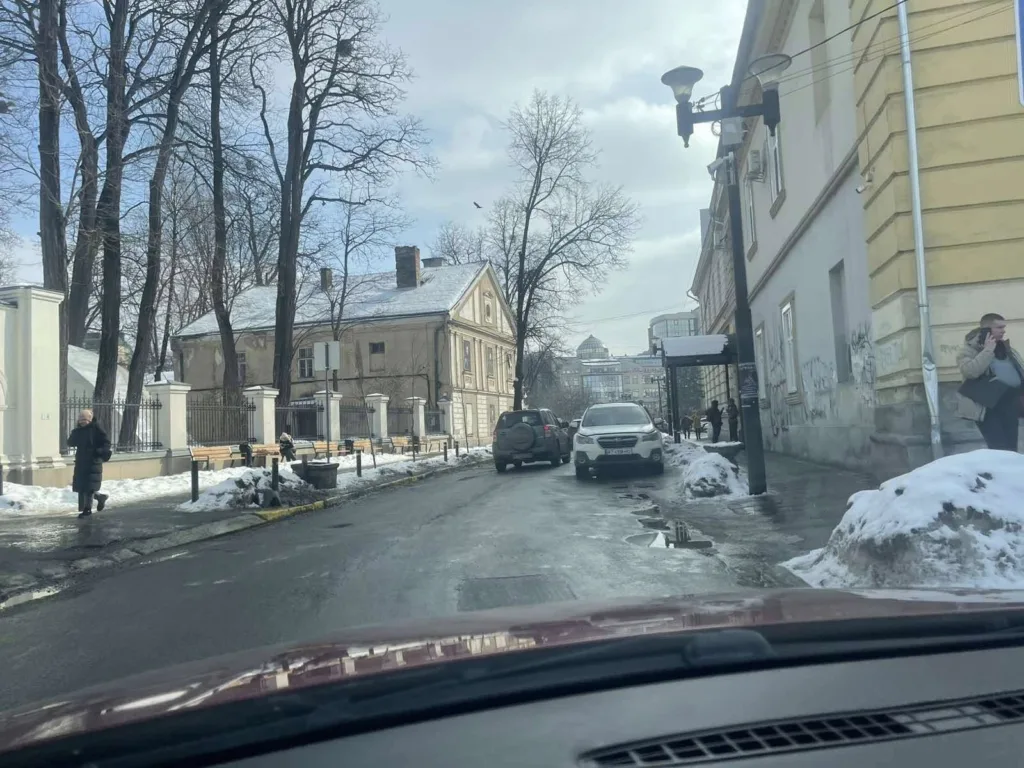 Засніжена міська вулиця з автомобілями та пішоходами