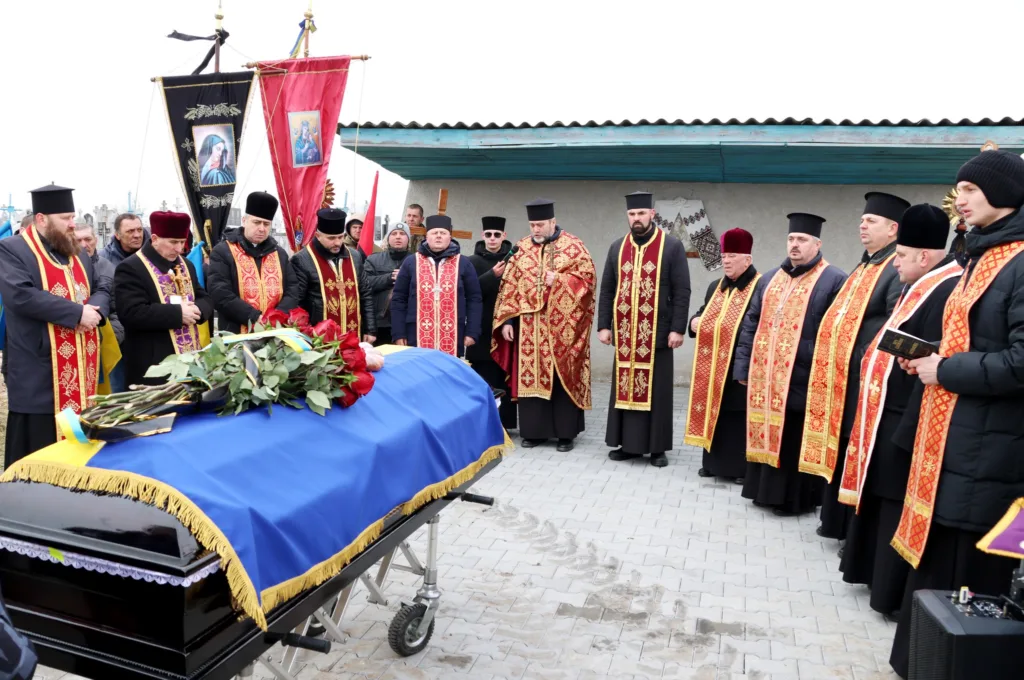 Священники проводять похоронну церемонію біля труни.