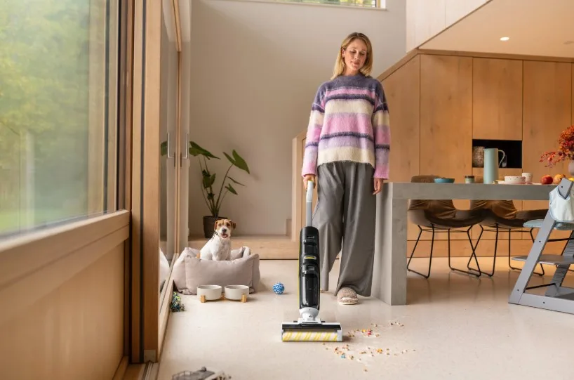 Жінка пилососить підлогу вдома поруч із собакою