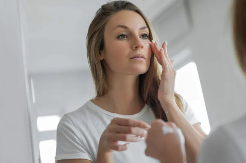 Жінка наносить крем на обличчя перед дзеркалом