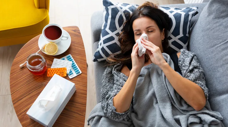 Жінка хворіє вдома, лежить із хусткою на дивані