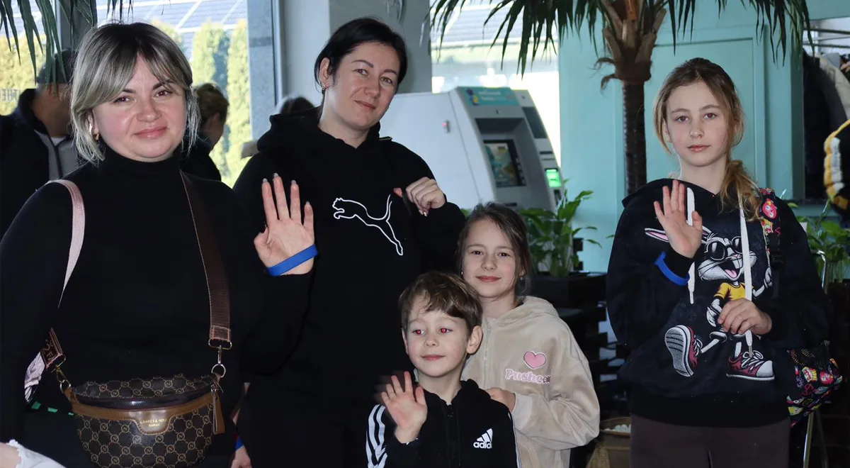 Група людей усміхається та махає рукою