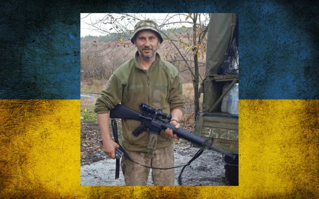 Український військовий з гвинтівкою на фоні прапора