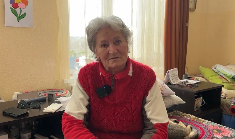 Літня жінка сидить у кімнаті біля вікна