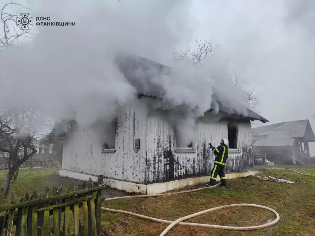 Пожежник гасить палаючий будинок із димом