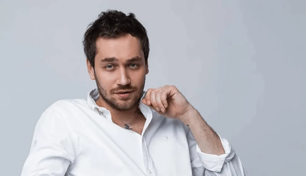 Чоловік у білій сорочці позує перед камерою