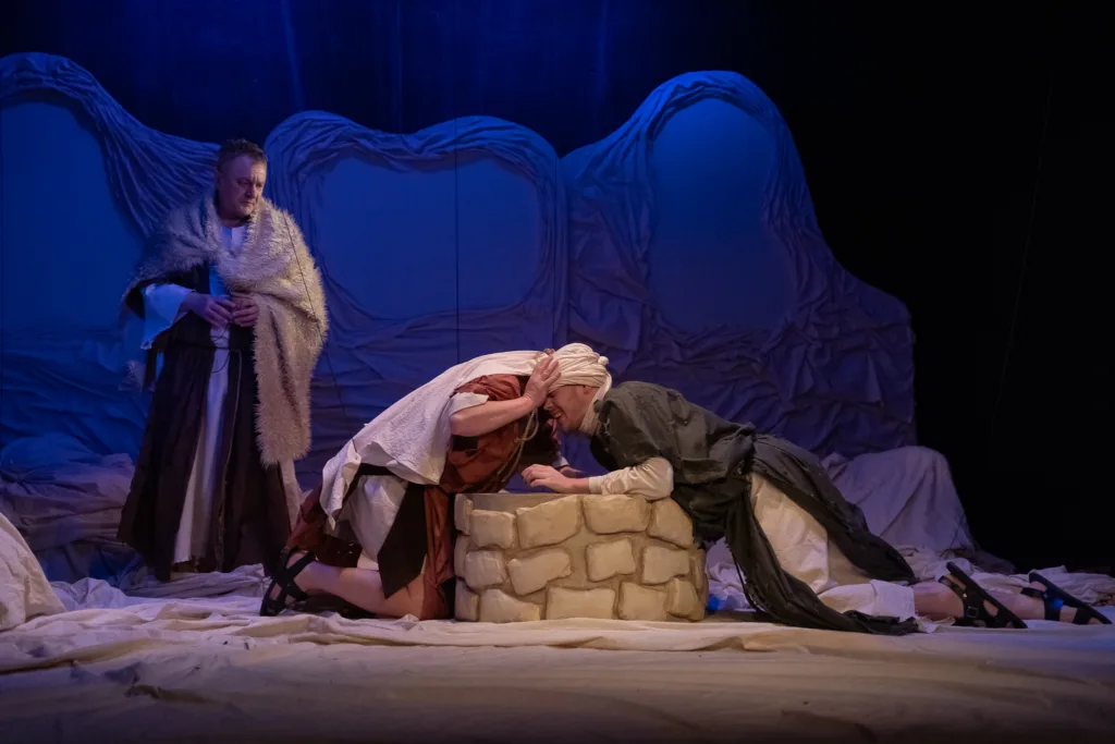 Сцена театральної вистави з трьома акторами біля колодязя