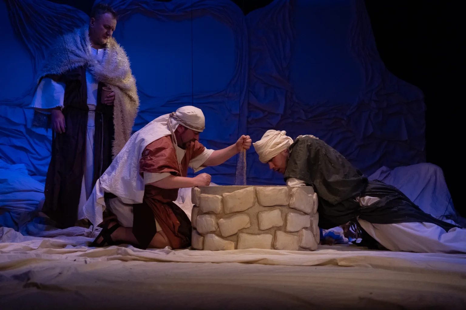 Театральна сцена з трьома акторами біля колодязя