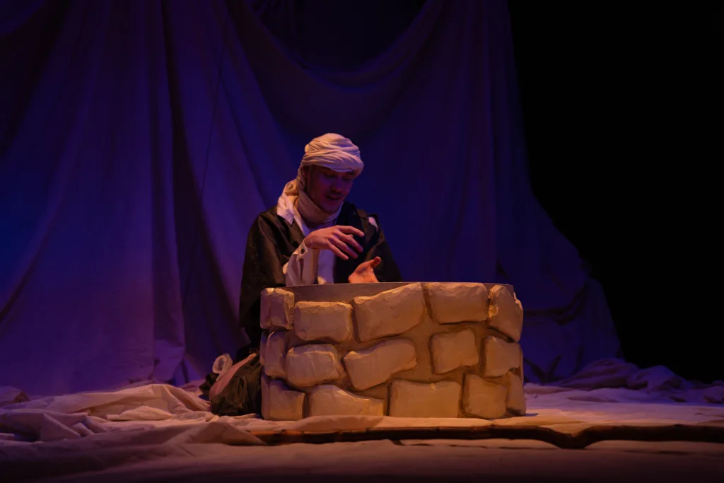 Актор біля колодязя на театральній сцені