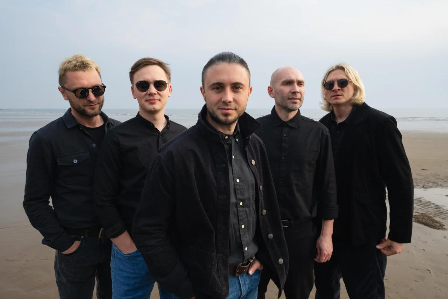 П’ятеро чоловіків у чорному стоять на пляжі