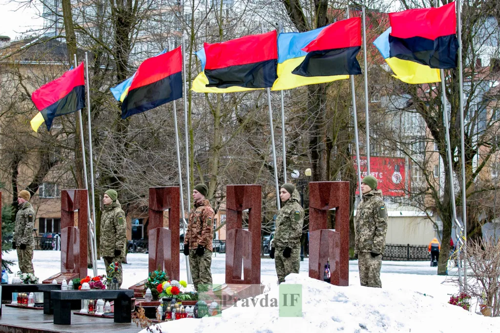 Військові стоять біля меморіалу з прапорами України