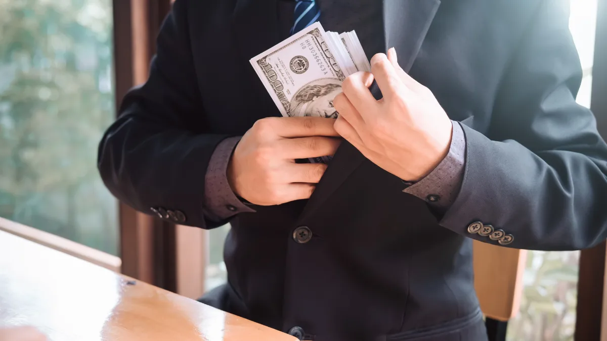 Бізнесмен кладе долари в кишеню піджака