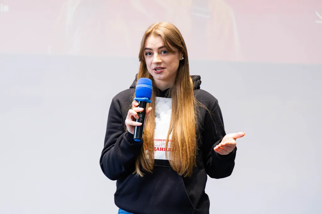 Молода жінка говорить у мікрофон на сцені