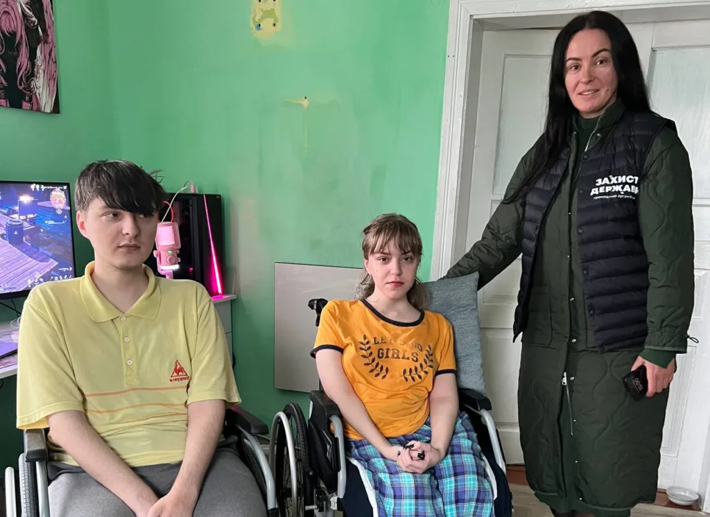 Двоє людей у візках та волонтерка в кімнаті