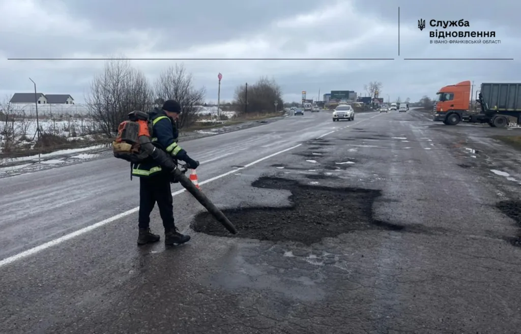 Робітник ремонтує ями на дорозі взимку