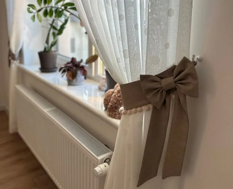 Біла фіранка з коричневим бантом біля вікна