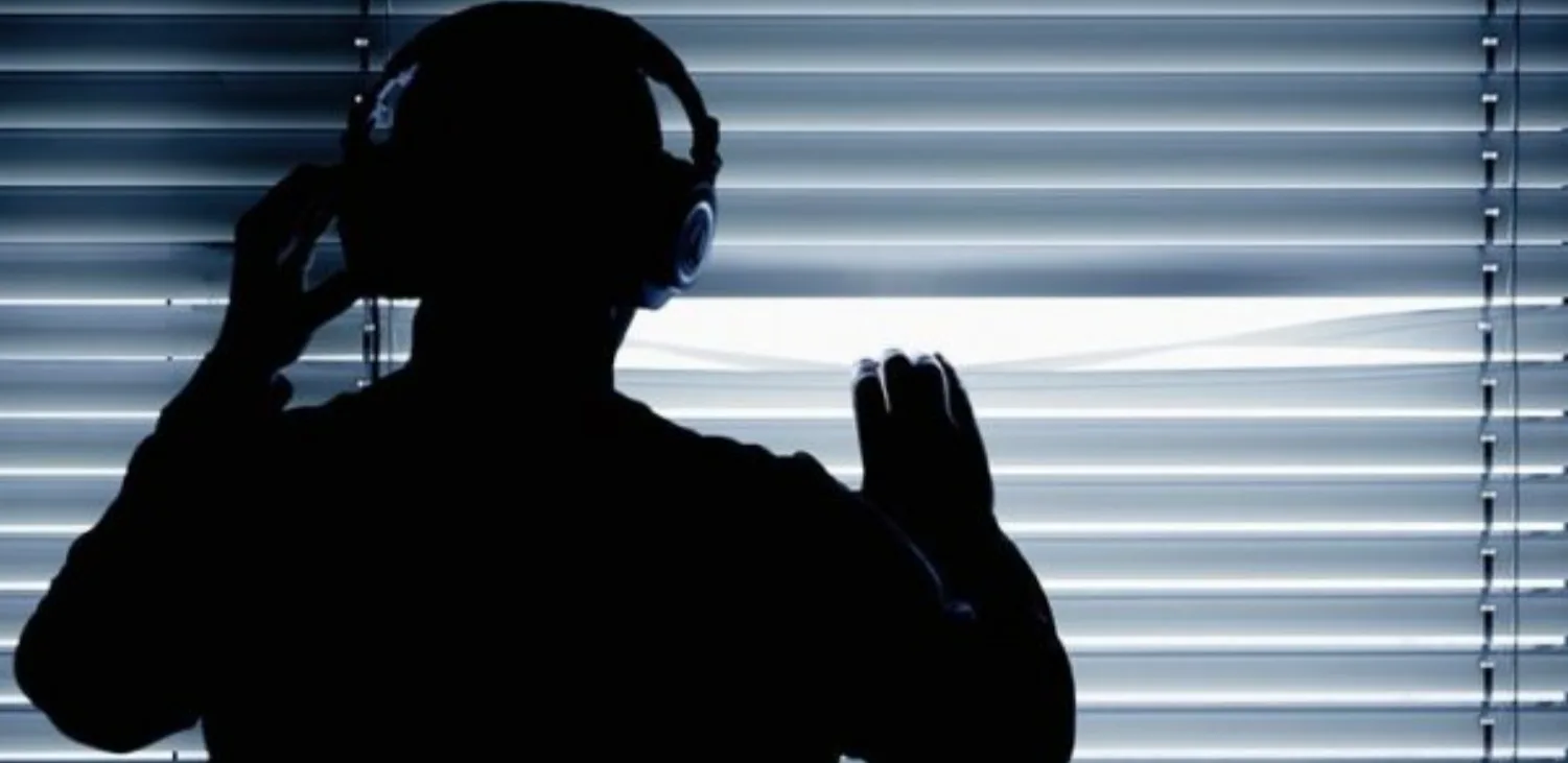 Людина у навушниках дивиться через жалюзі