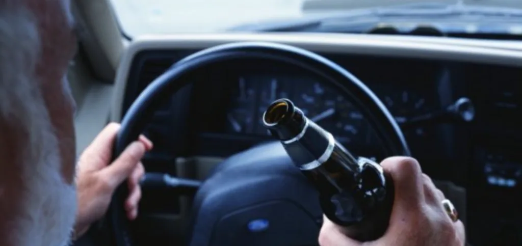 Людина тримає пляшку за кермом автомобіля