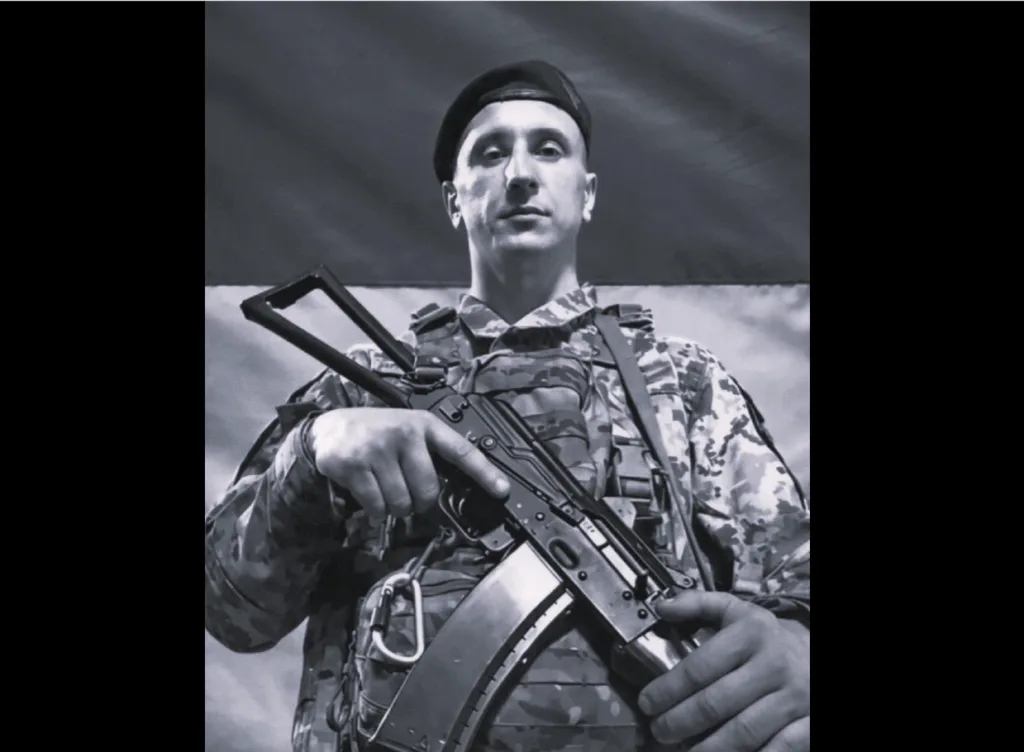 Український військовий у формі з прапором позаду