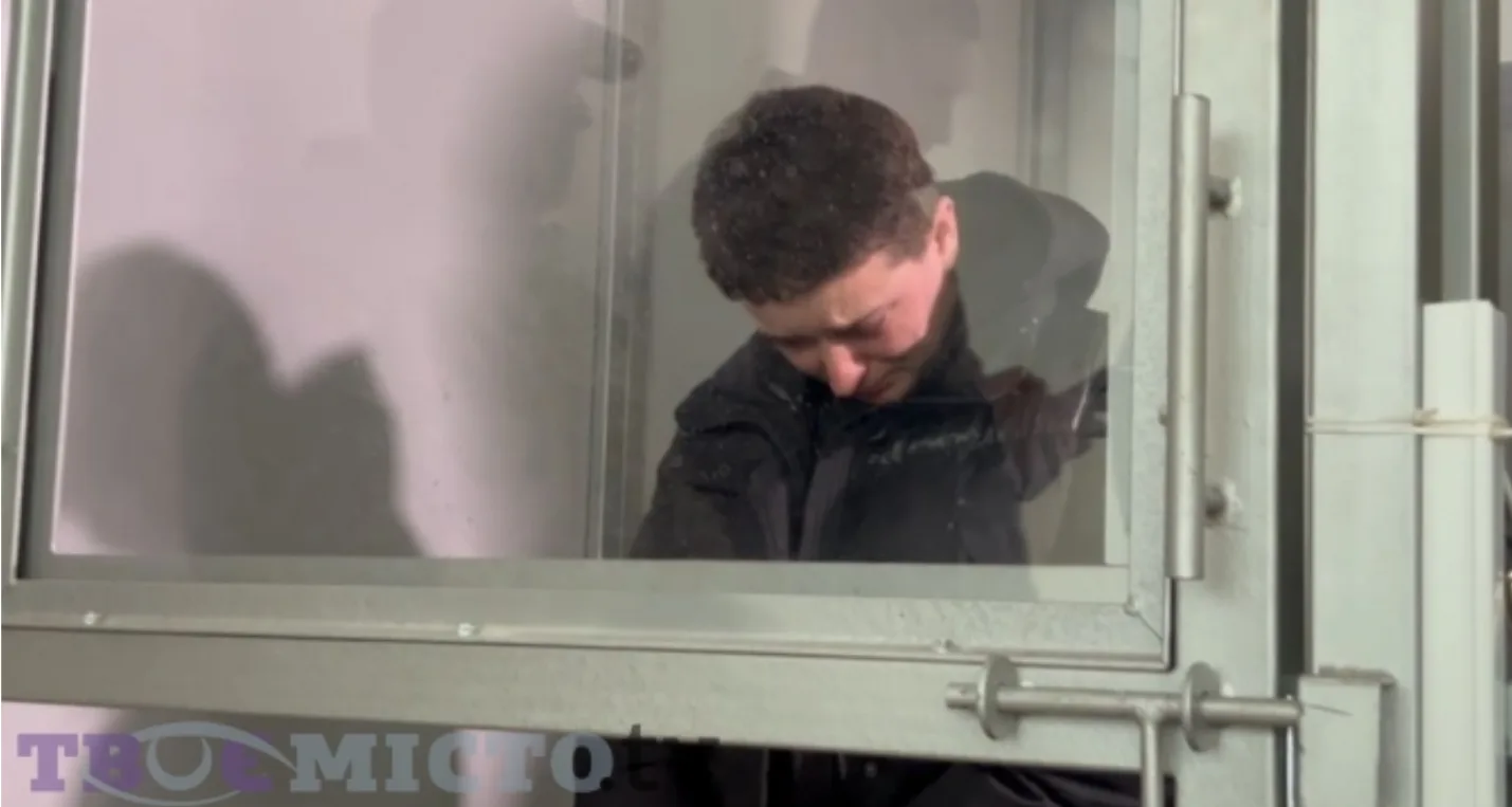 Людина стоїть у скляній кабіні суду