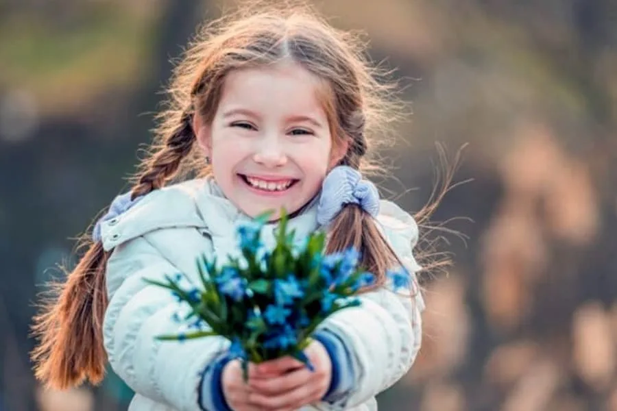 Усміхнена дівчинка тримає букет синіх квітів