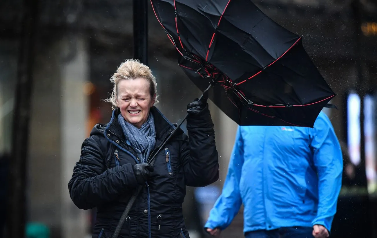 Жінка бореться з вітром і зламаною парасолькою