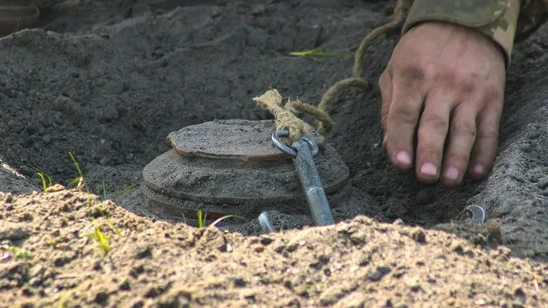 Військовий розміновує міну в землі