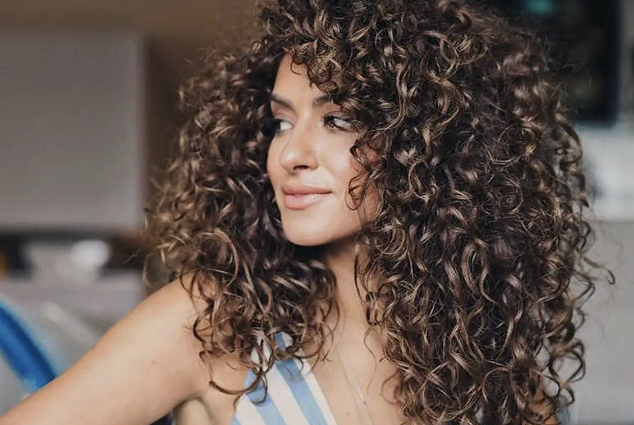 Жінка з довгим кучерявим волоссям усміхається