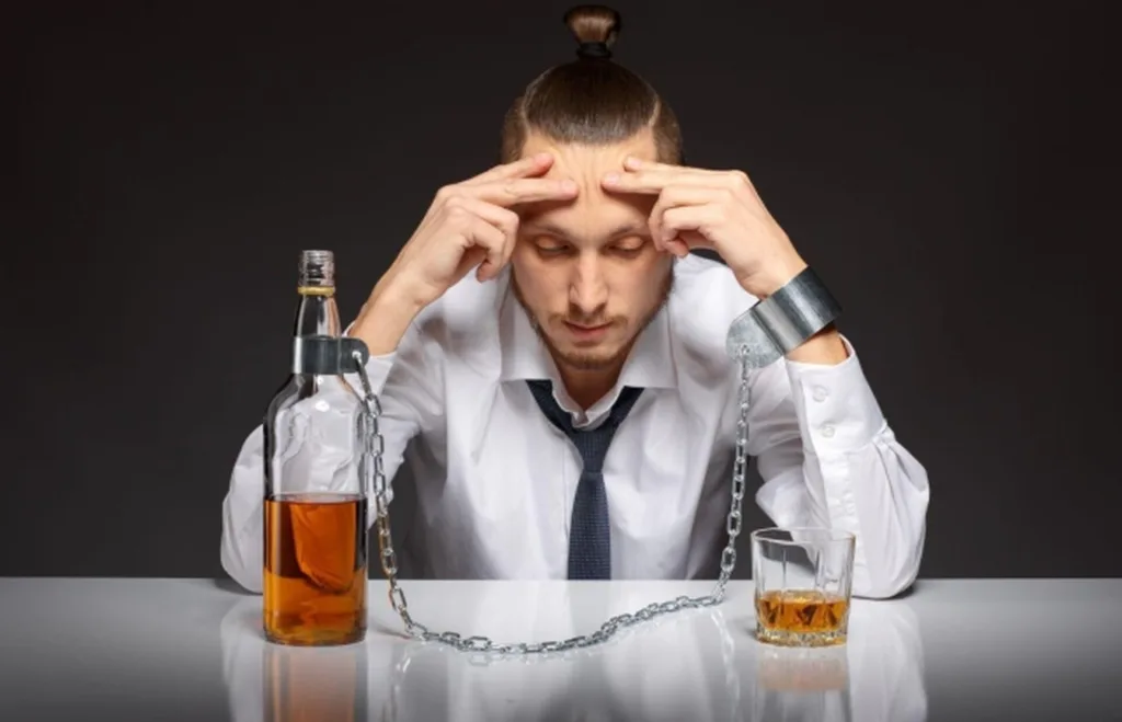 Чоловік у кайданках поруч із пляшкою алкоголю