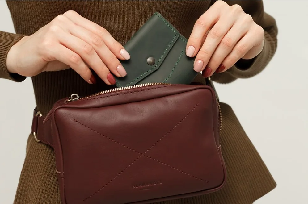 Жінка кладе гаманець у шкіряну сумку